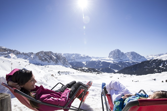 Skifahrerinnen sonnen sich im Liegestuhl auf Seceda, im Hintergrund die Berglandschaft